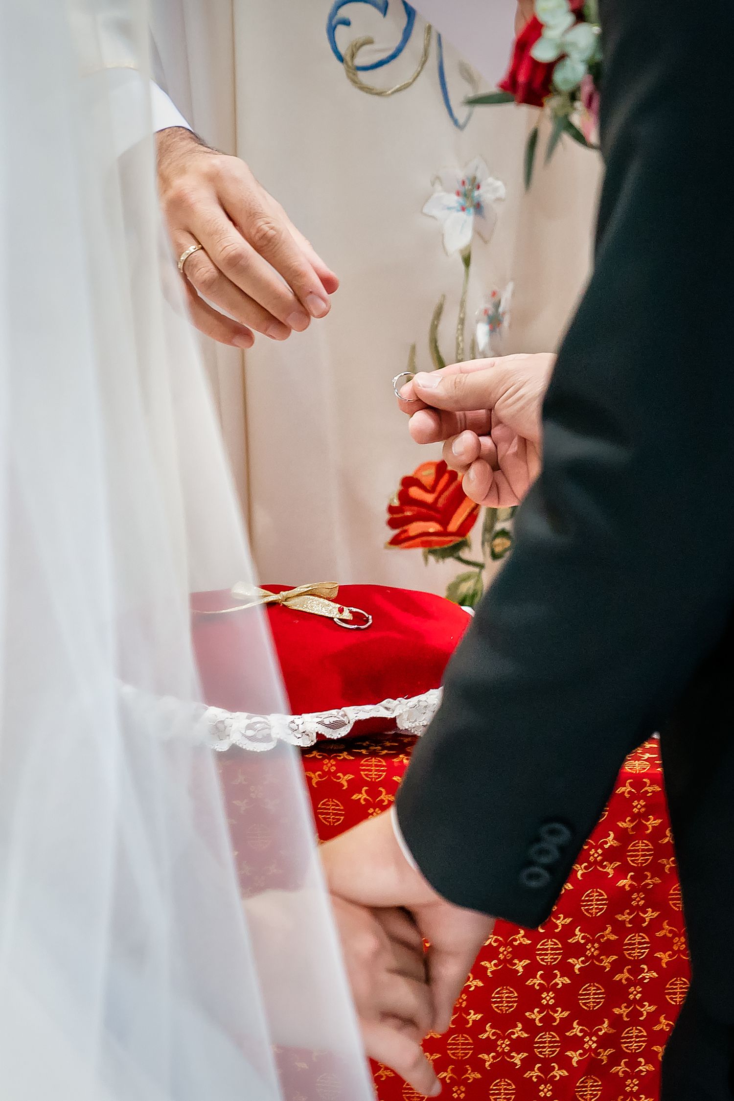 Close-up of wedding rings being exchanged on a red decorative pillow during ceremony.