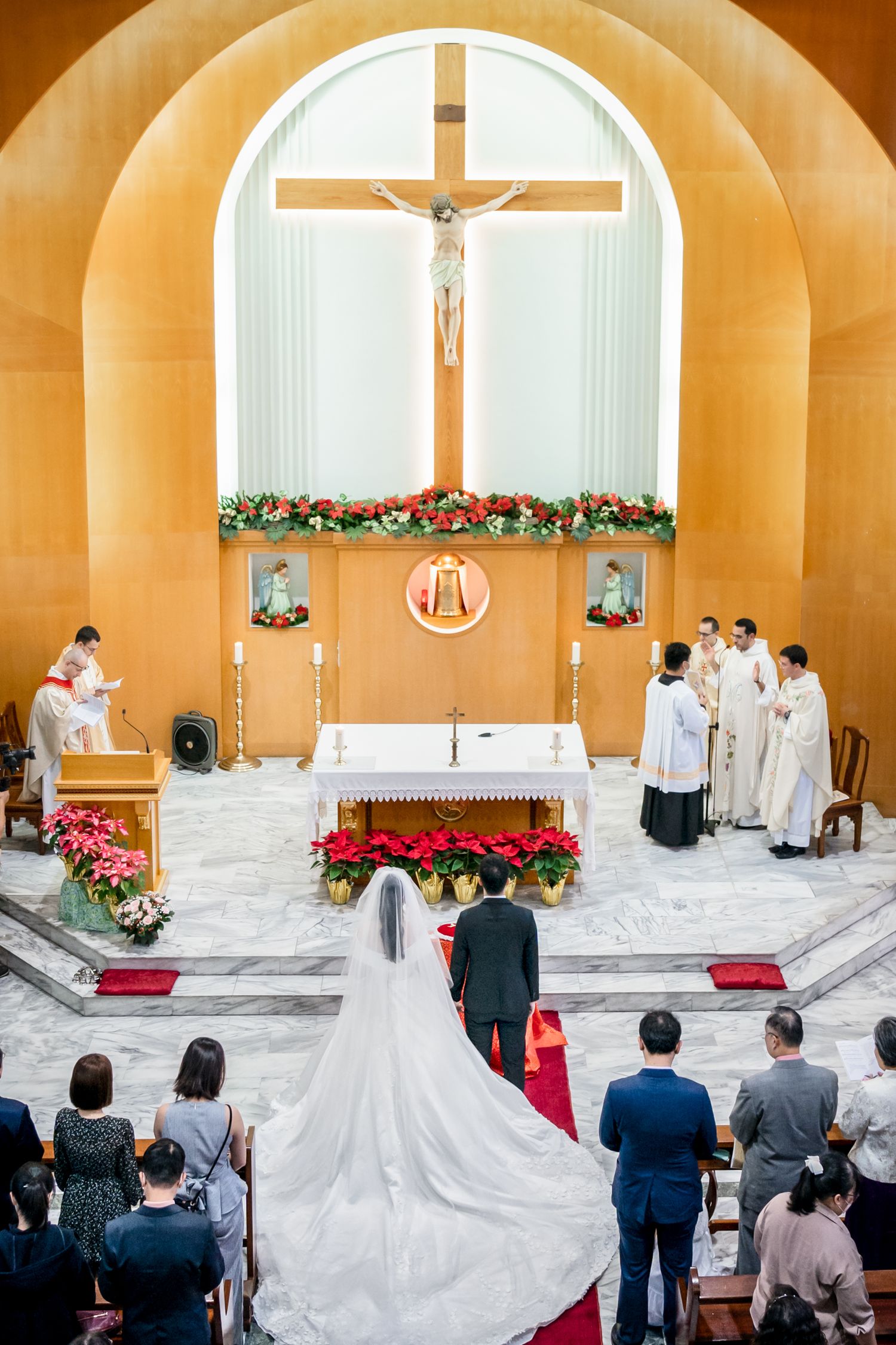 Wedding ceremony at Catholic church altar decorated with poinsettias and cross.