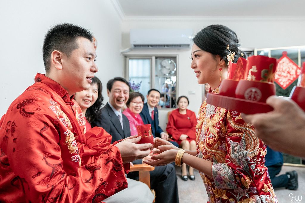 Couple participates in traditional Chinese tea ceremony with guests watching in background.