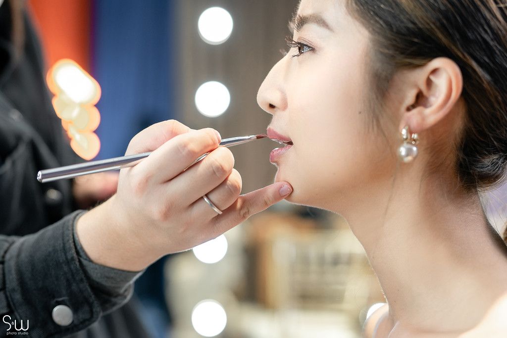 Professional makeup application in progress with soft lighting and pearl earring detail.