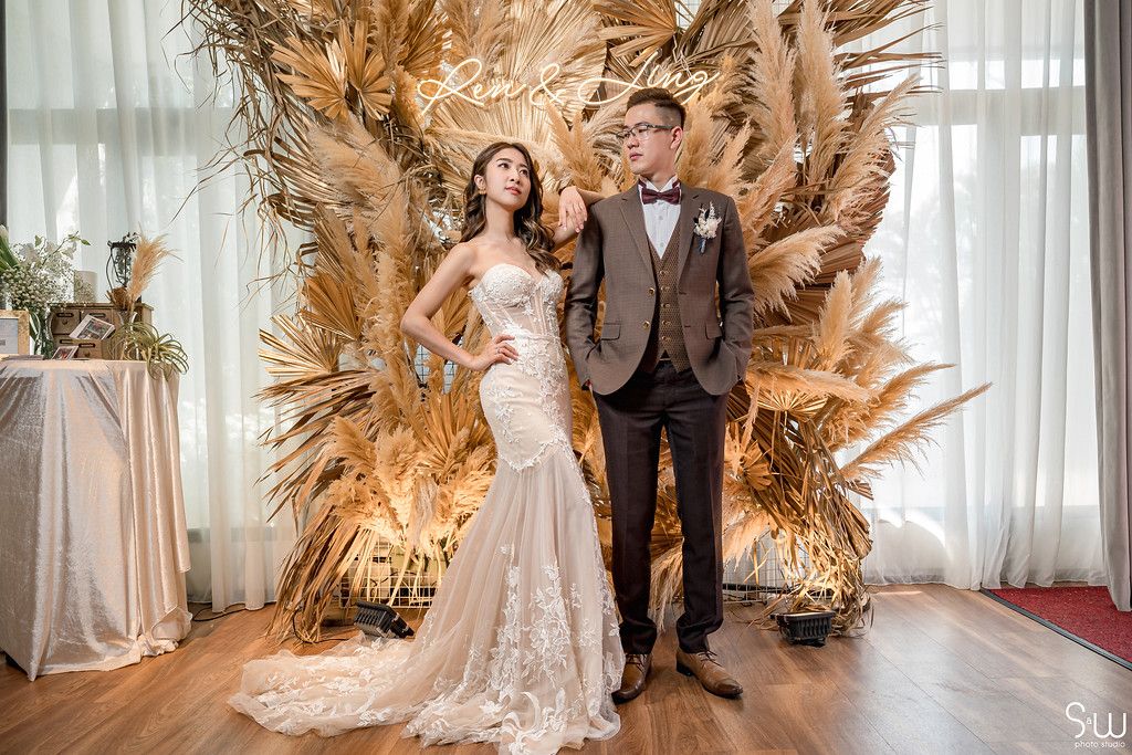 Glamorous wedding portrait with couple standing against golden dried grass backdrop.