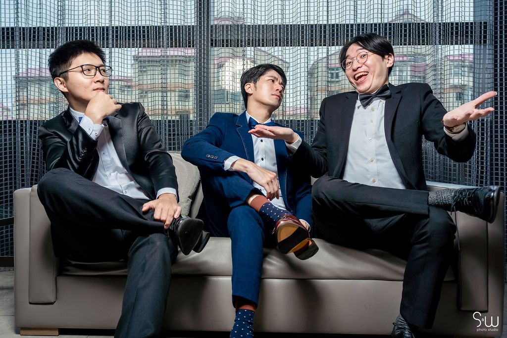 Three friends in formal attire share a casual moment laughing together on a couch.