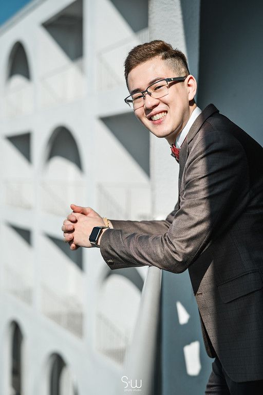 Portrait of a person in formal attire smiling against architectural backdrop.