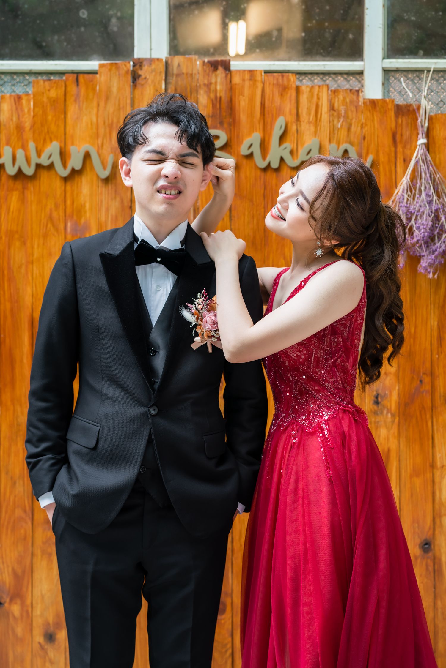 Playful formal photo session with red gown and black tuxedo against wooden background.