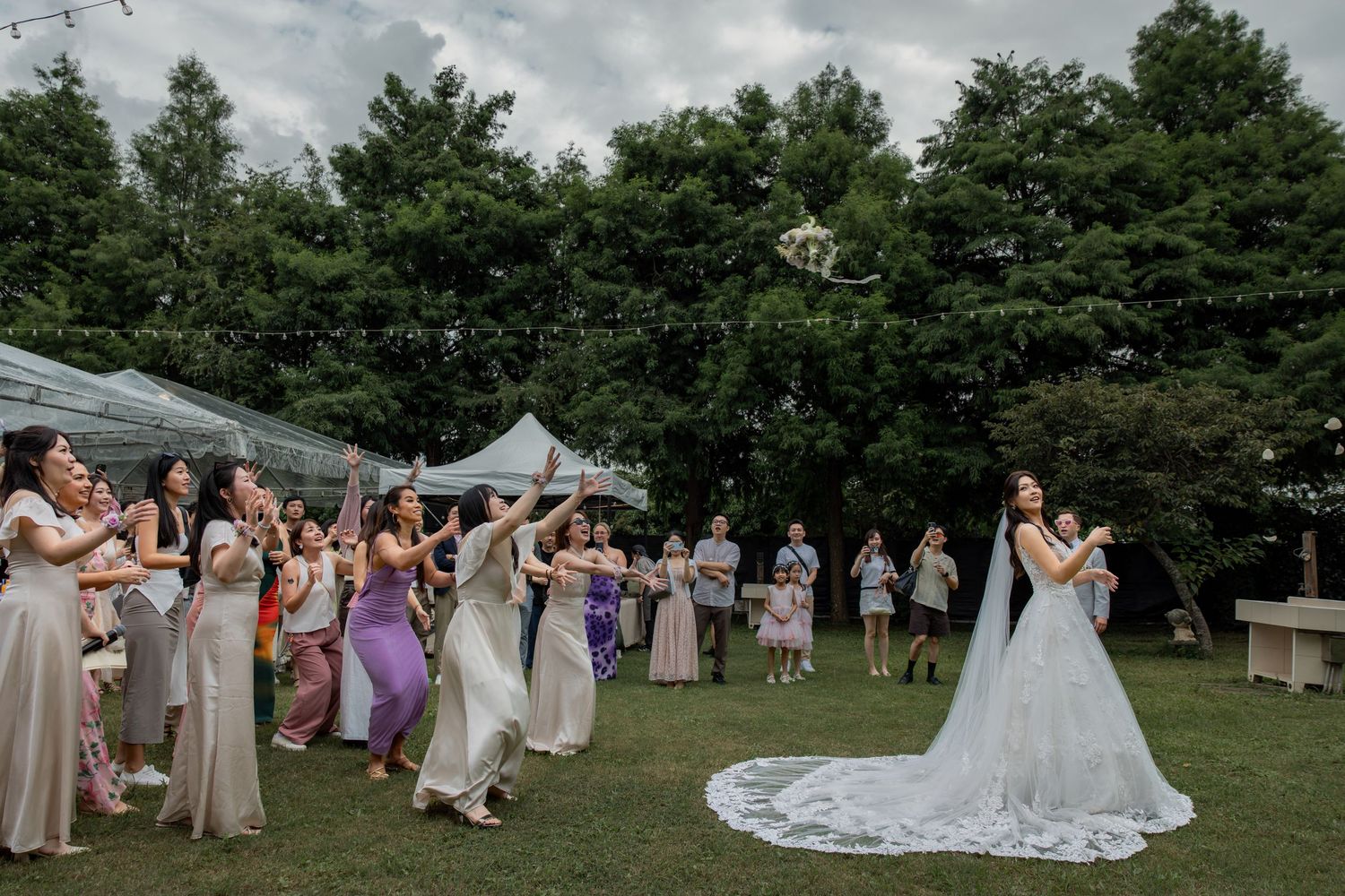 Bride tossing bouquet to excited bridesmaids in pastel dresses on lush green lawn at outdoor wedding reception.台北婚禮攝影
婚禮攝影師
戶外婚禮
婚禮紀實
婚攝推薦
台