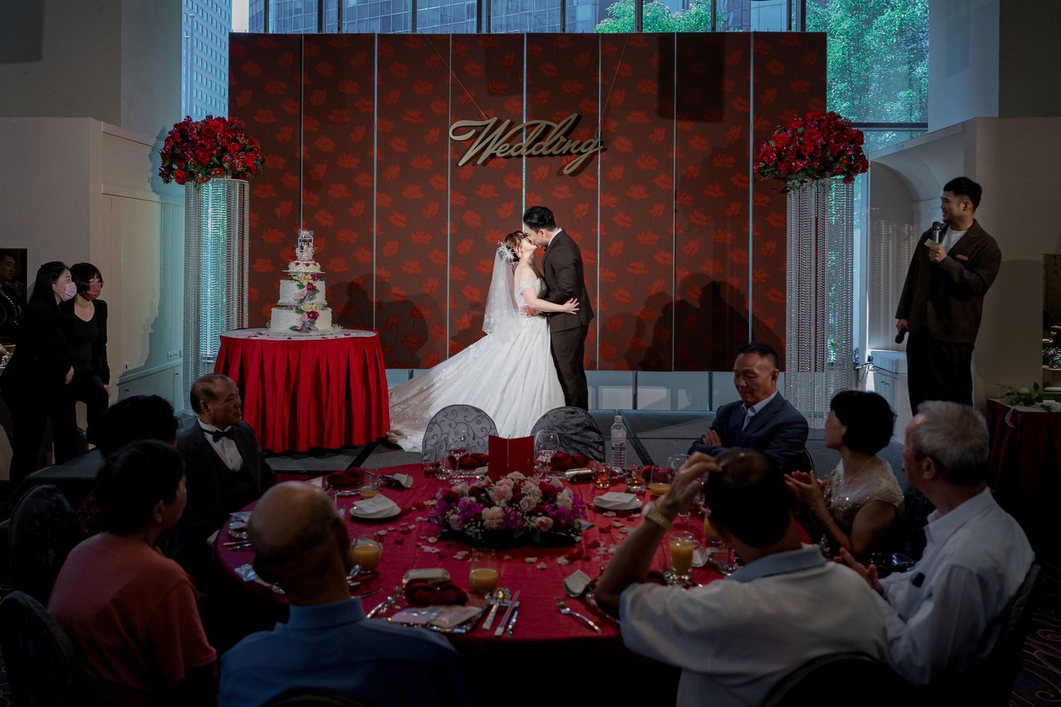 A wedding reception event space with red decor and multiple tables set up for guests during a celebration.