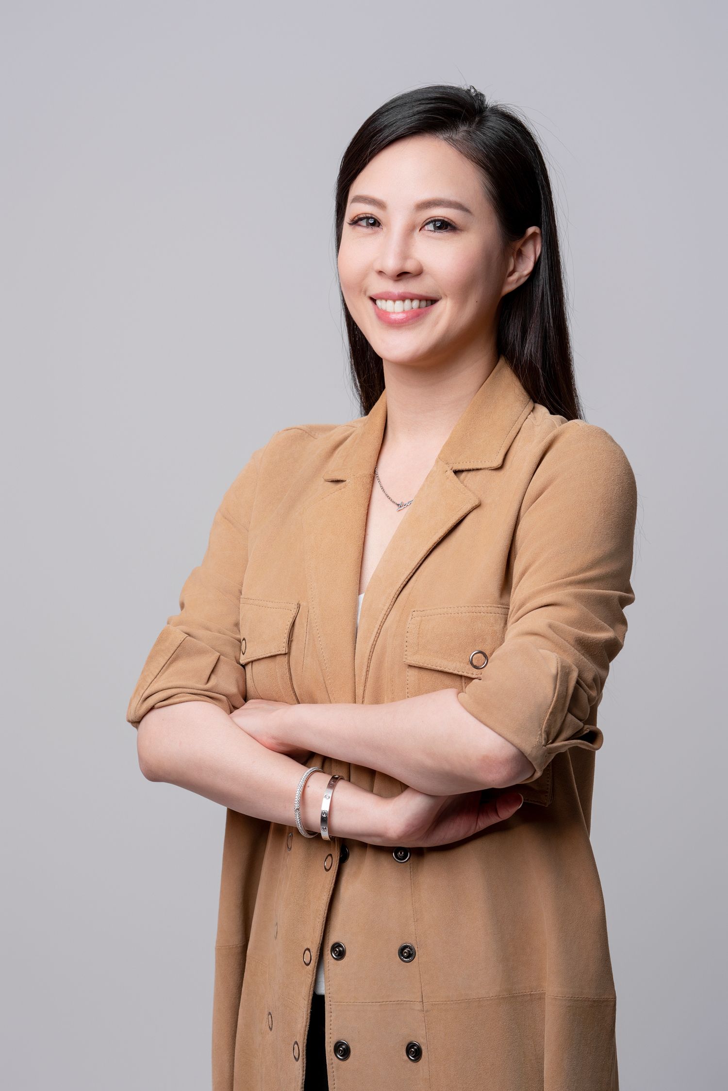 Professional studio portrait of someone wearing a tan double-breasted blazer against a light gray background.