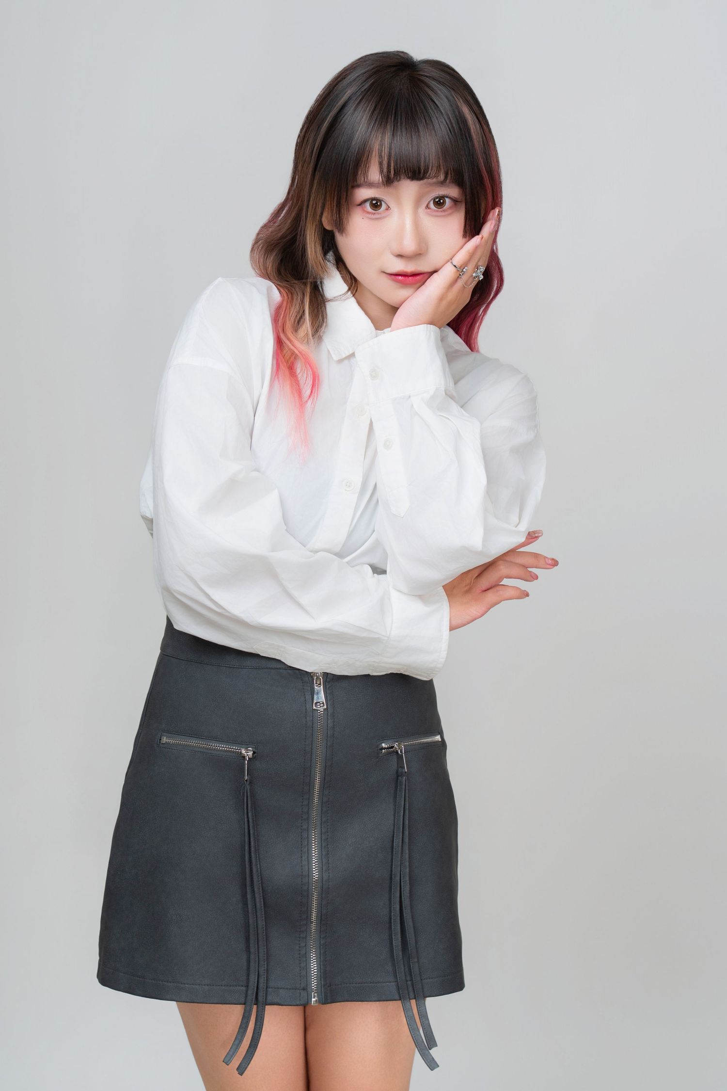 A series of fashion photos showing a person in a white blouse and dark pleated miniskirt against a gray background.