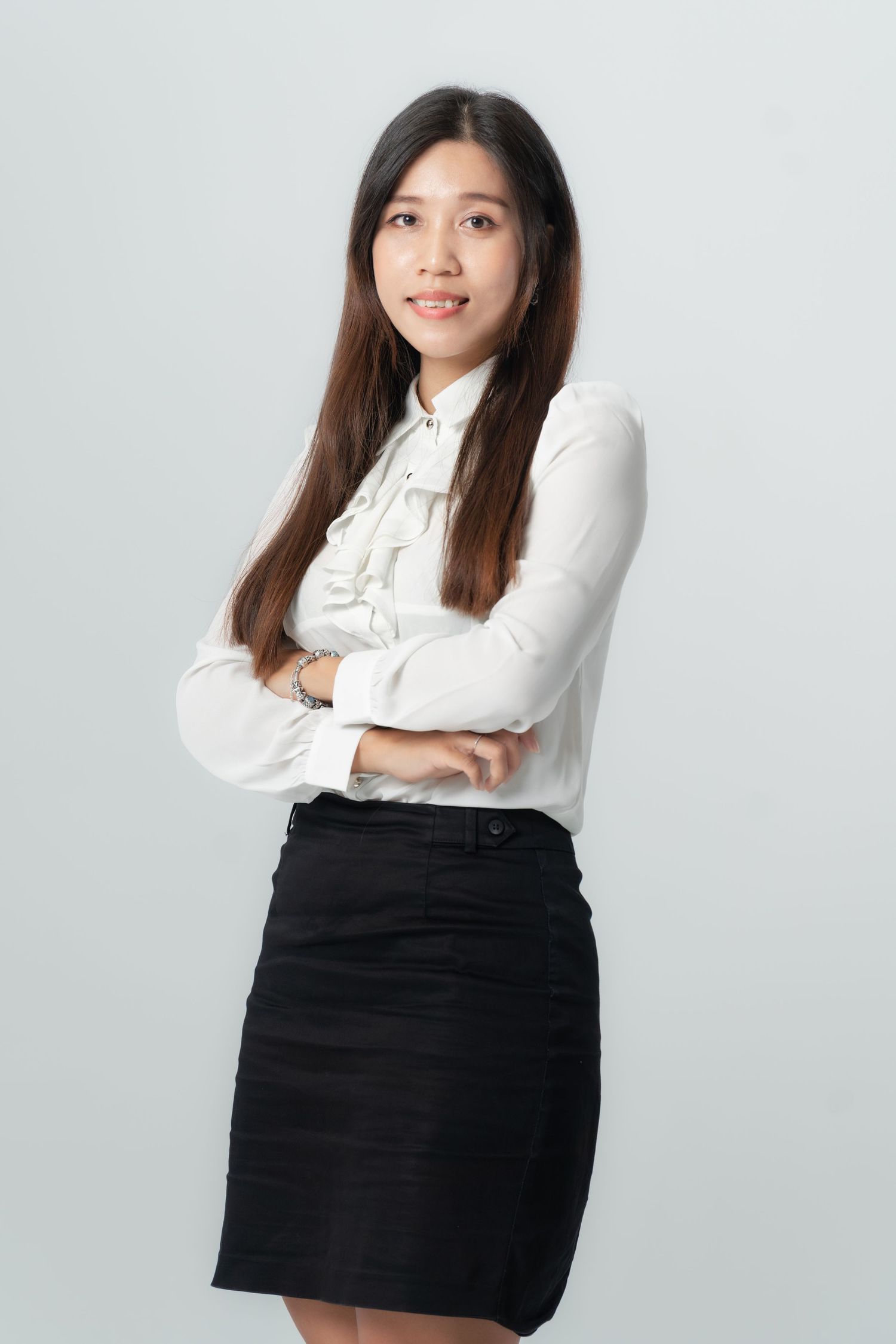 Professional studio portrait of a person in a white button-down shirt and black skirt posing against a light background.