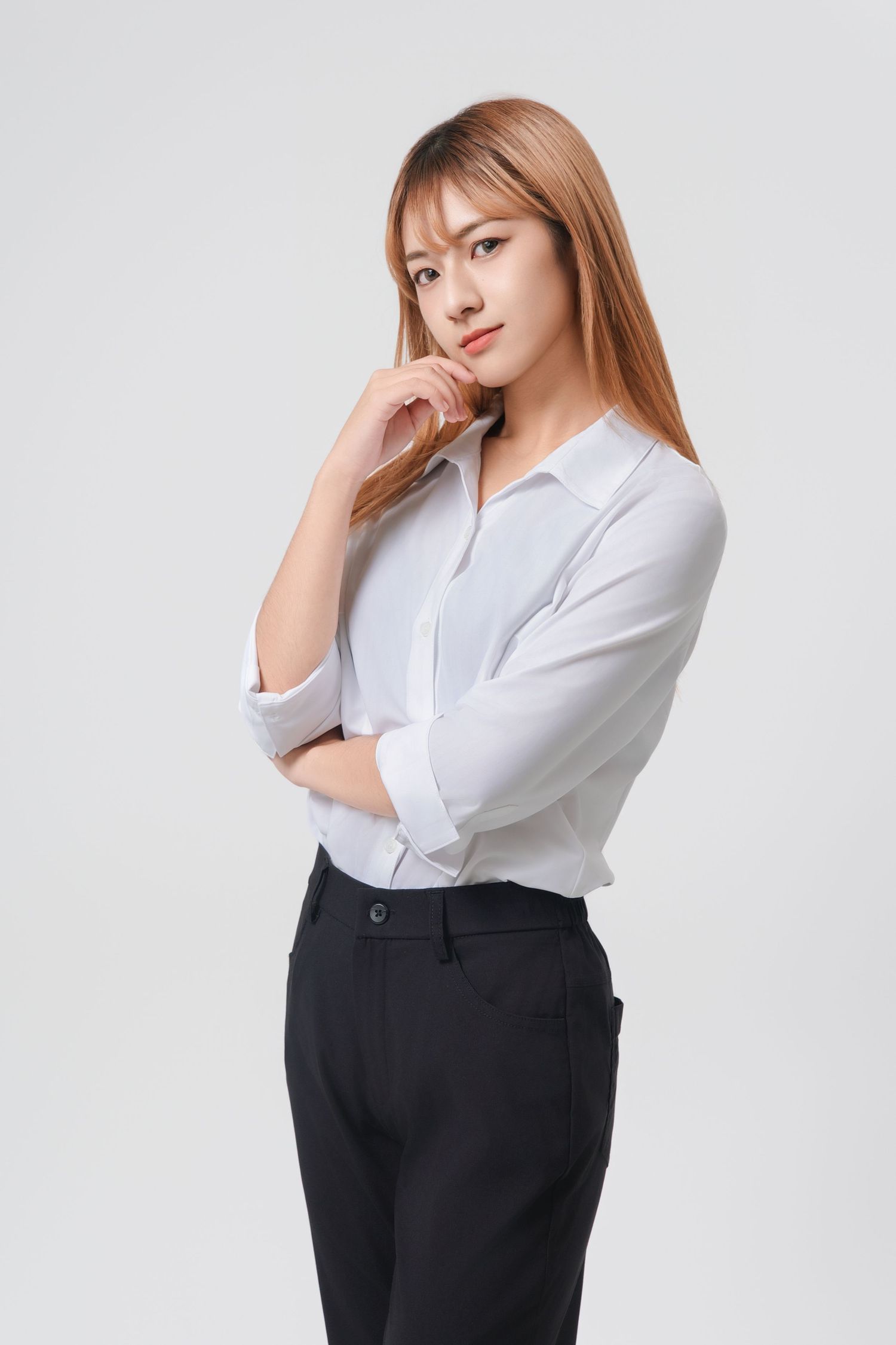 Professional woman in white button-up shirt and black pants poses against light background in business portrait series.
