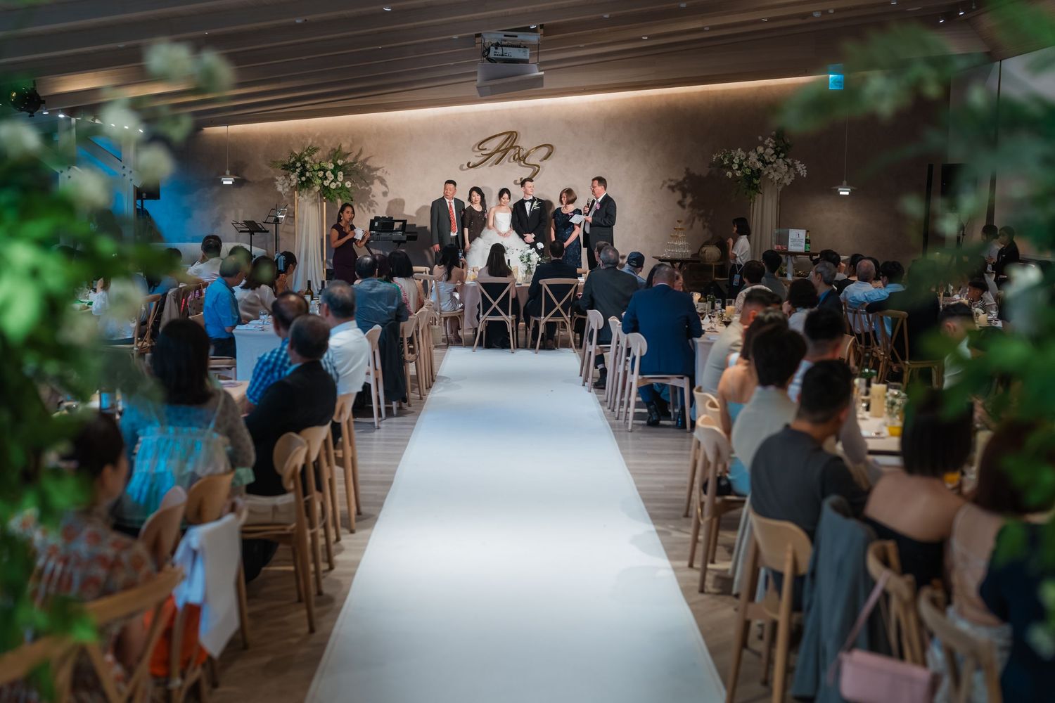 Indoor wedding ceremony setup with white aisle runner and wooden chairs in a modern venue lit by soft lighting.