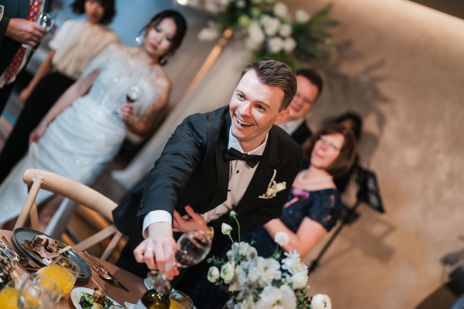 Organic floral table centerpieces with eucalyptus leaves decorate an elegant wedding reception at night.