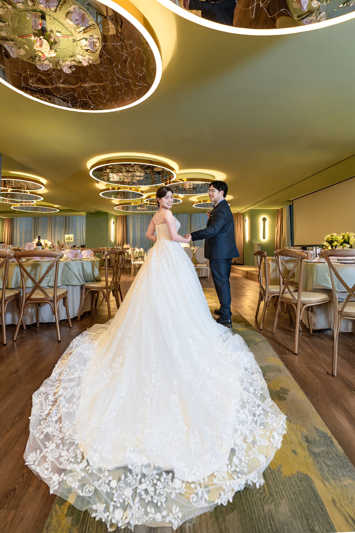 A stunning white lace wedding gown with a dramatic cathedral train displayed in an elegant reception venue.