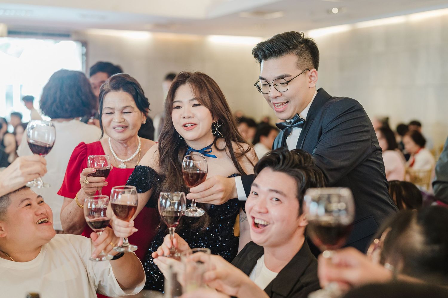 A group of people enjoying wine and raising their glasses in celebration at an elegant indoor gathering.