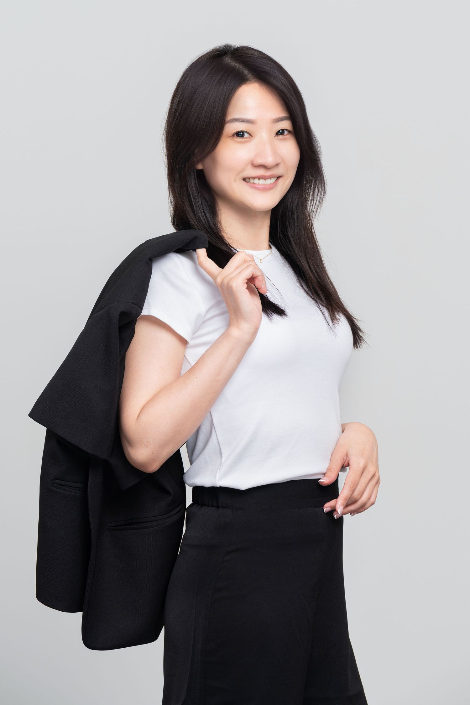 Professional business attire photo with white top, black skirt and blazer against light grey studio background.