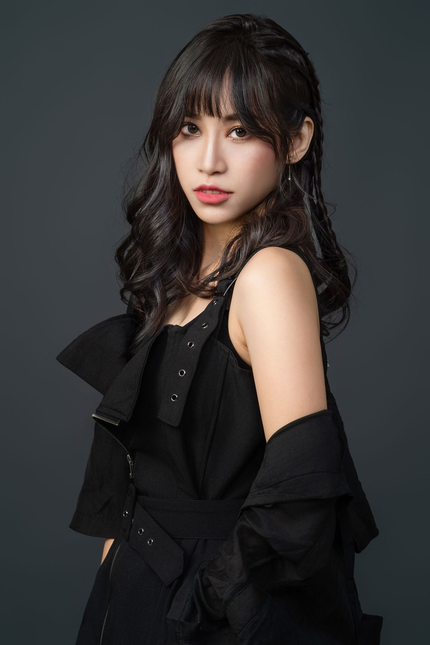 Professional portrait of a young woman in a black outfit with long dark wavy hair against a dark gray background.