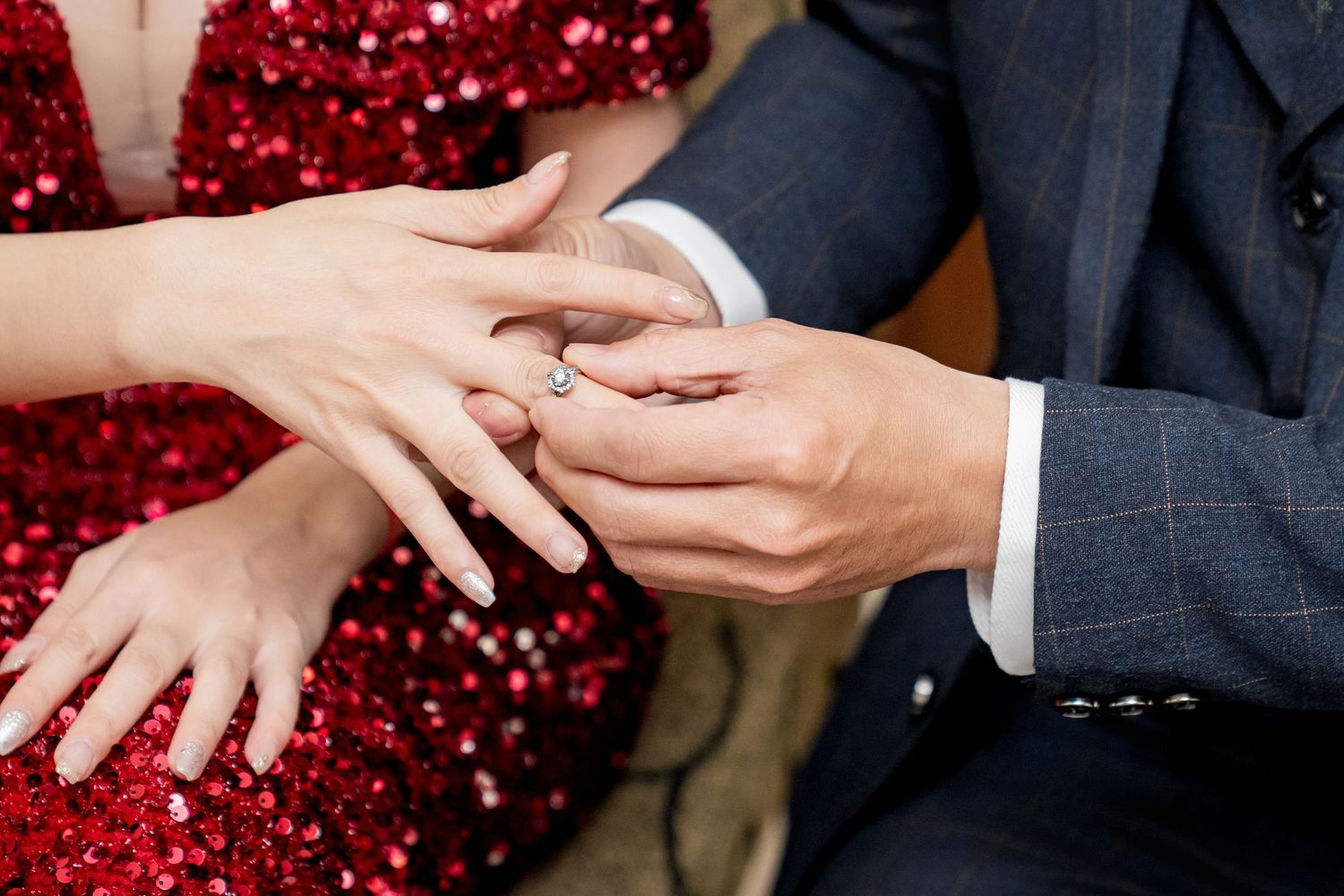Close-up shot of hands exchanging wedding rings during proposal with sparkly red background.