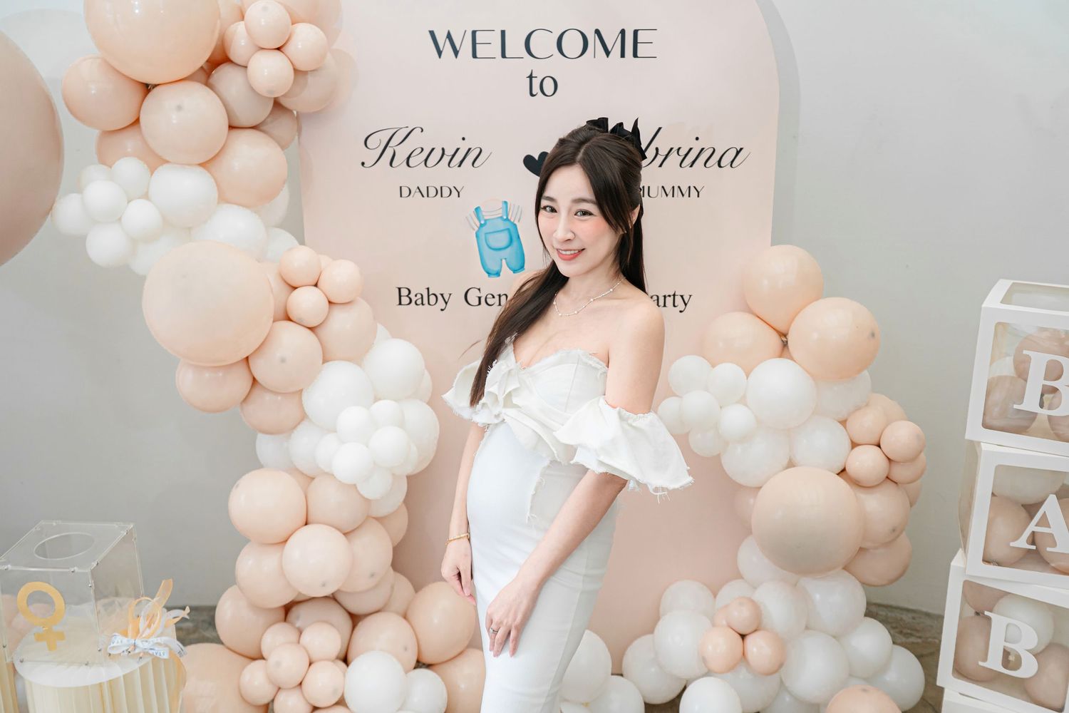 A baby shower celebration setup with peach and white balloon garlands, welcome signs, and elegant party decorations.