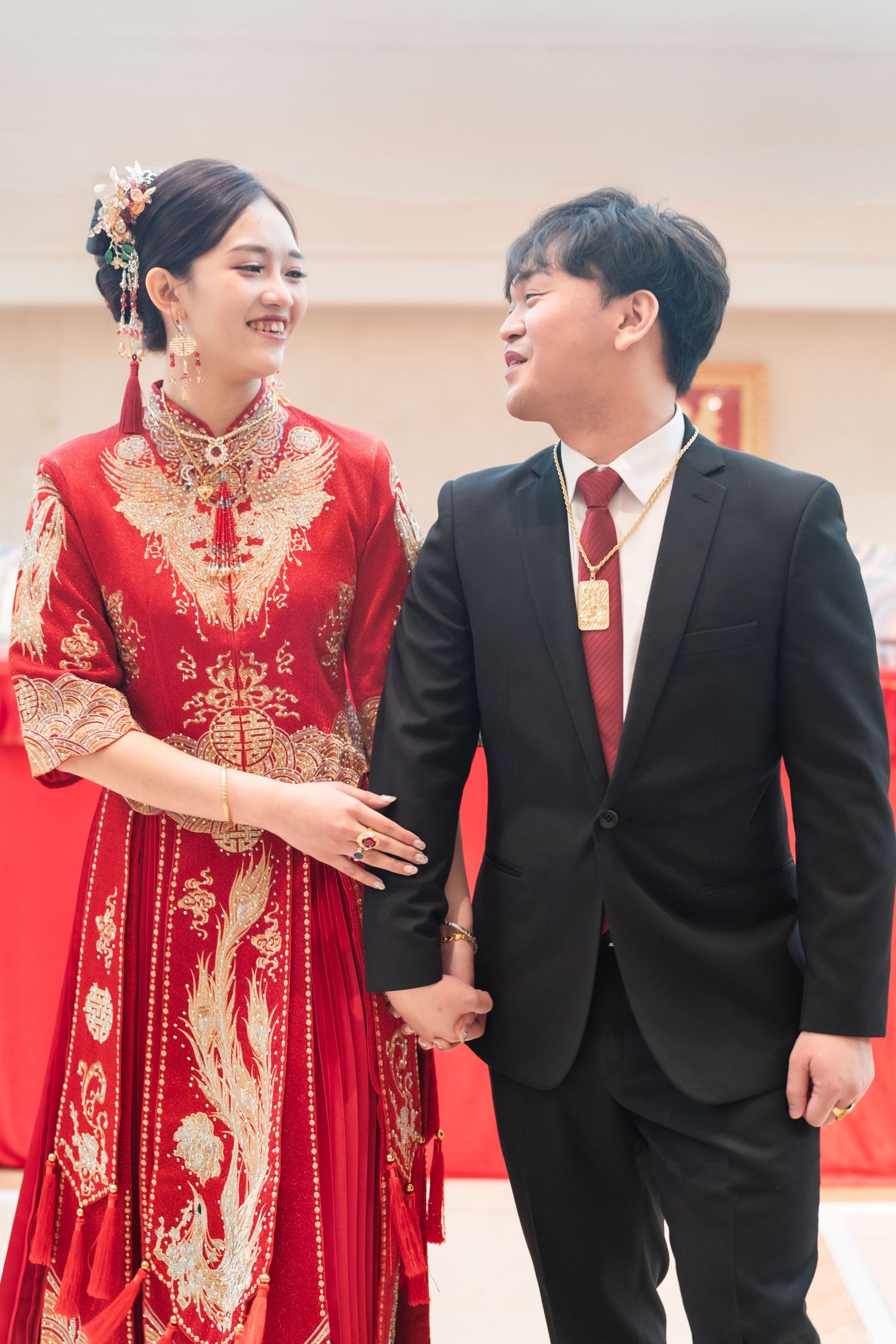 A couple shares a joyful moment, with the bride wearing a traditional red Chinese qipao wedding dress and gold embellishments.