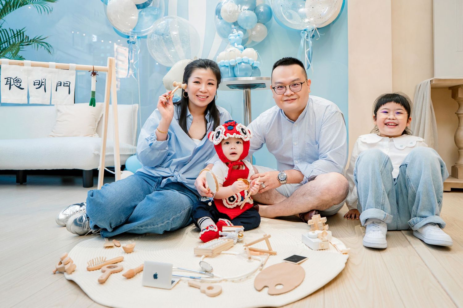 A family in matching blue outfits sits on the floor with toys and balloons for a fun indoor photoshoot.