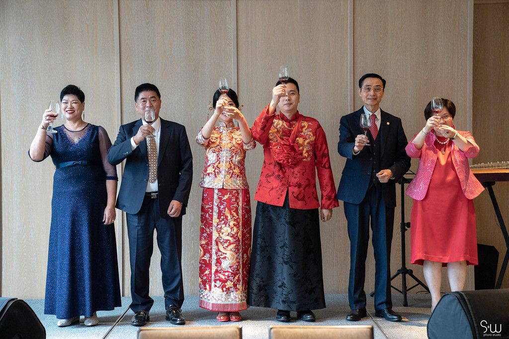 Wedding guests and couple in traditional Chinese attire pose together making heart gestures.
