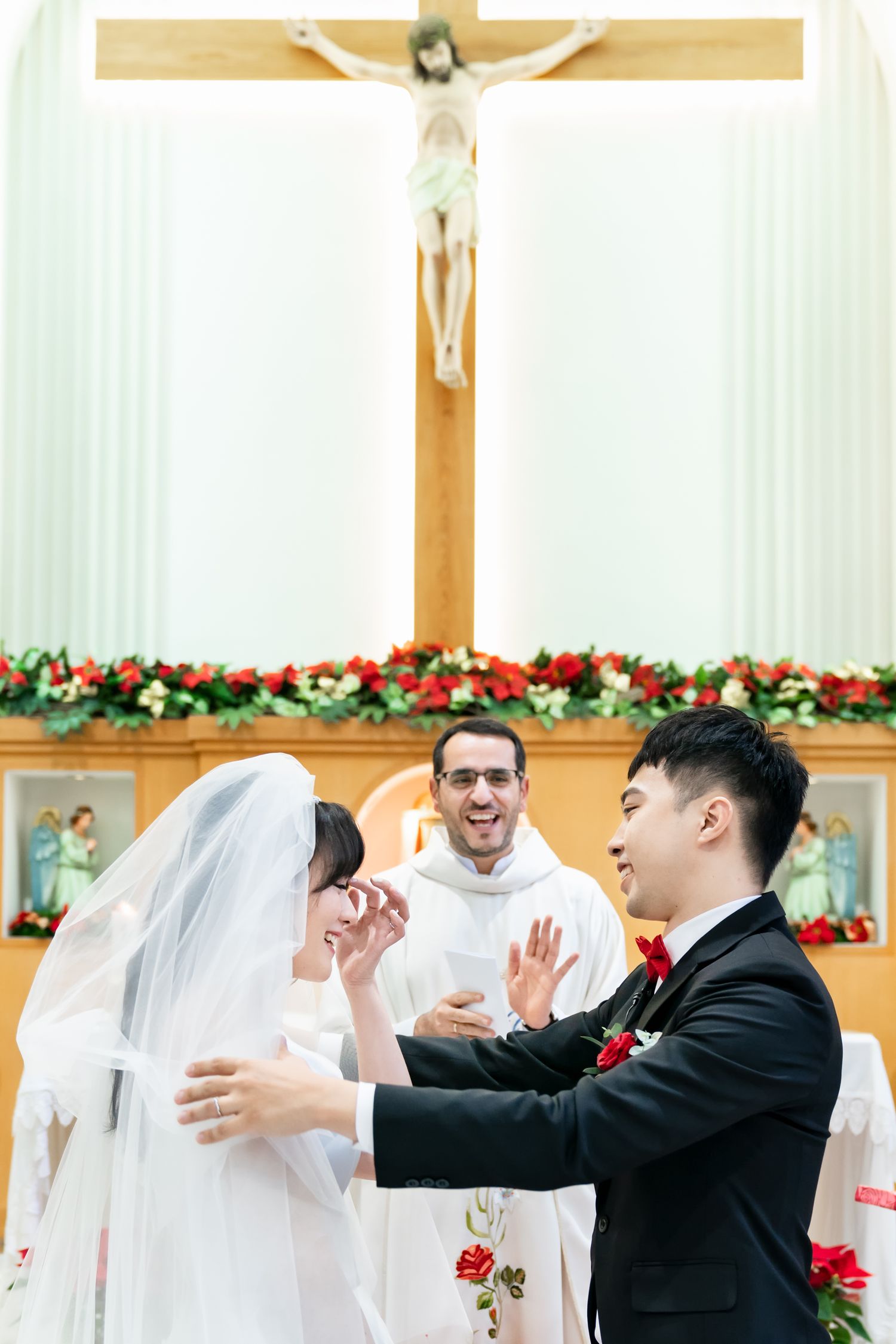 Emotional wedding ceremony moment in church with priest and decorative floral altar.