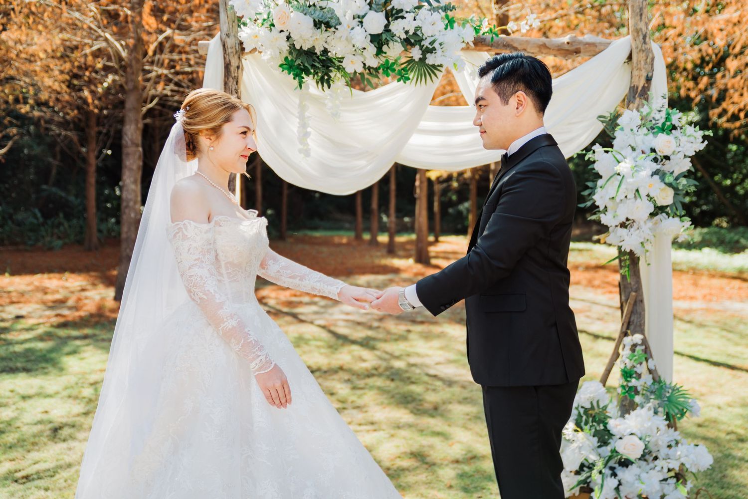 Bride and groom stand under floral arch during outdoor fall wedding ceremony.
