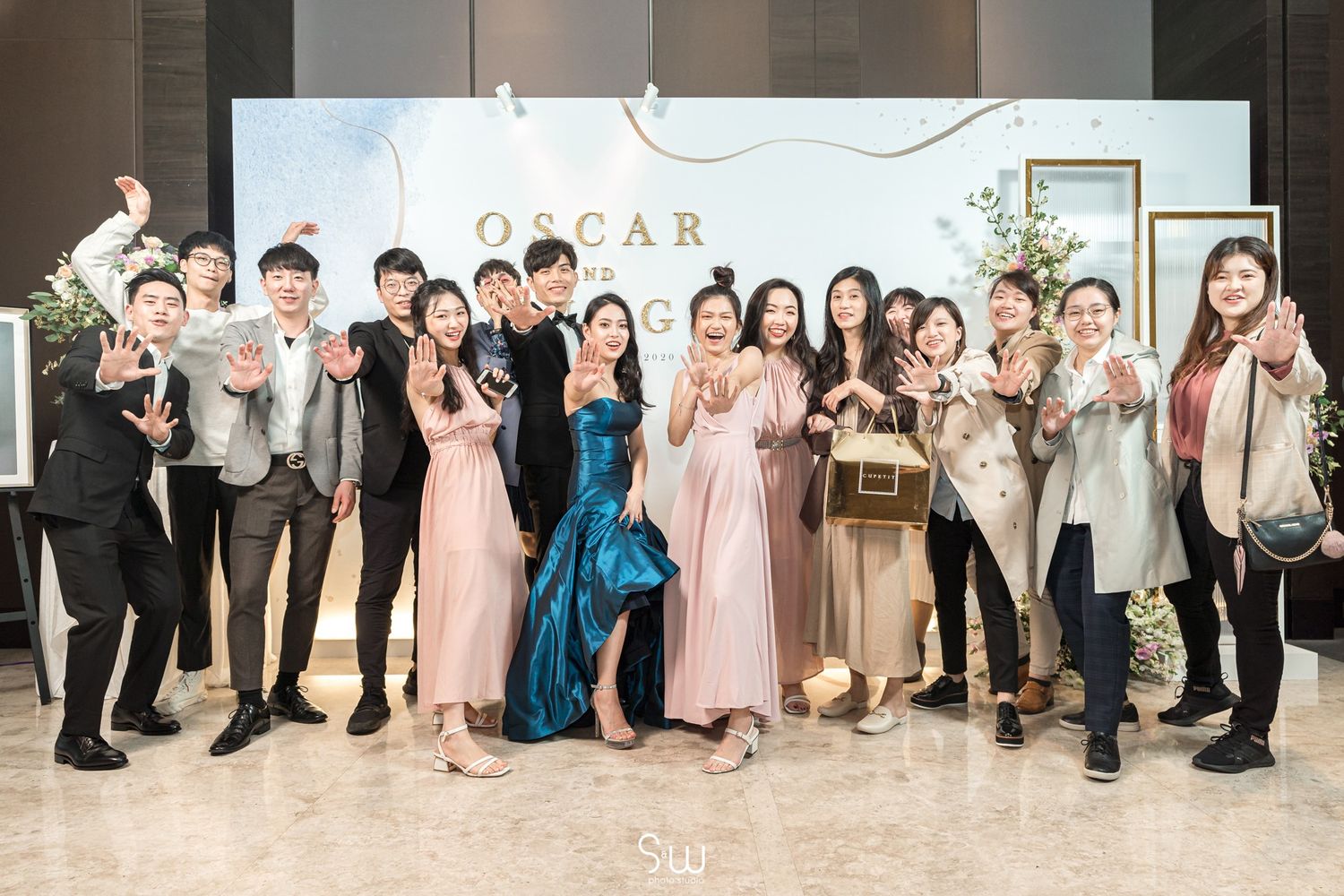 Large group photo of wedding party celebrating in front of Oscar-themed backdrop.