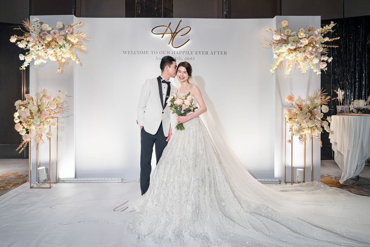 Elegant wedding photo backdrop with white panels, illuminated floral arrangements and a couple posing in formal attire.