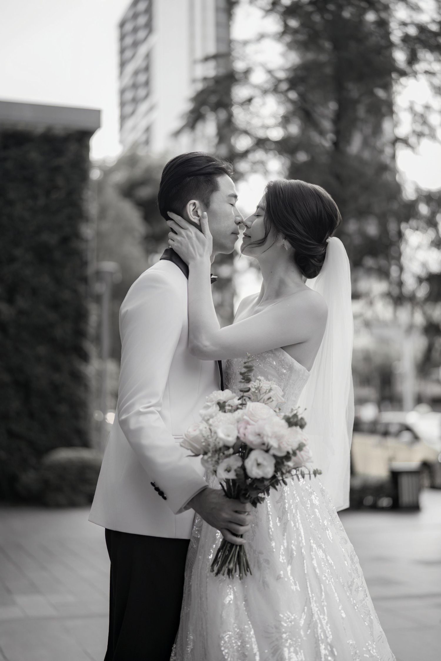 A tender moment between newlyweds sharing a kiss while holding a delicate pink and white floral bouquet.