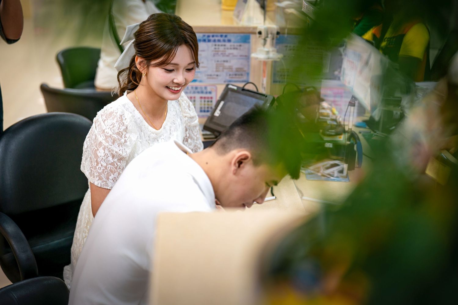 Wedding couple shares intimate moment framed by green foliage at outdoor celebration.