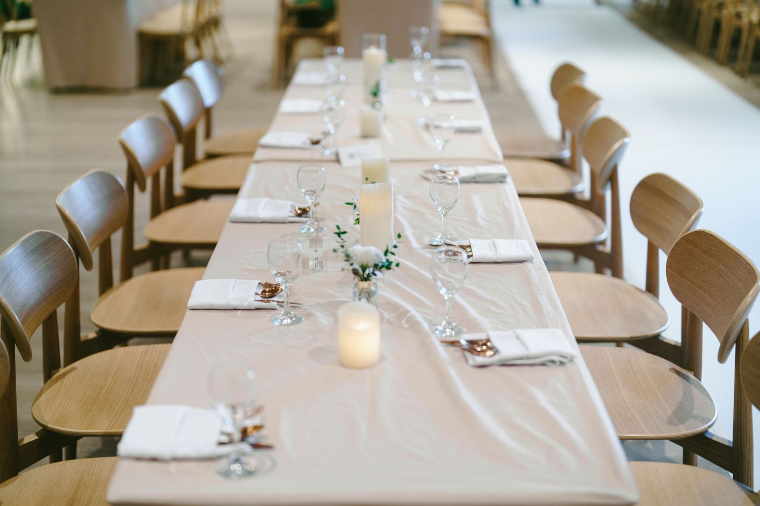 Long banquet tables with white linens and place settings extend through an elegant dining room ready for a formal event.