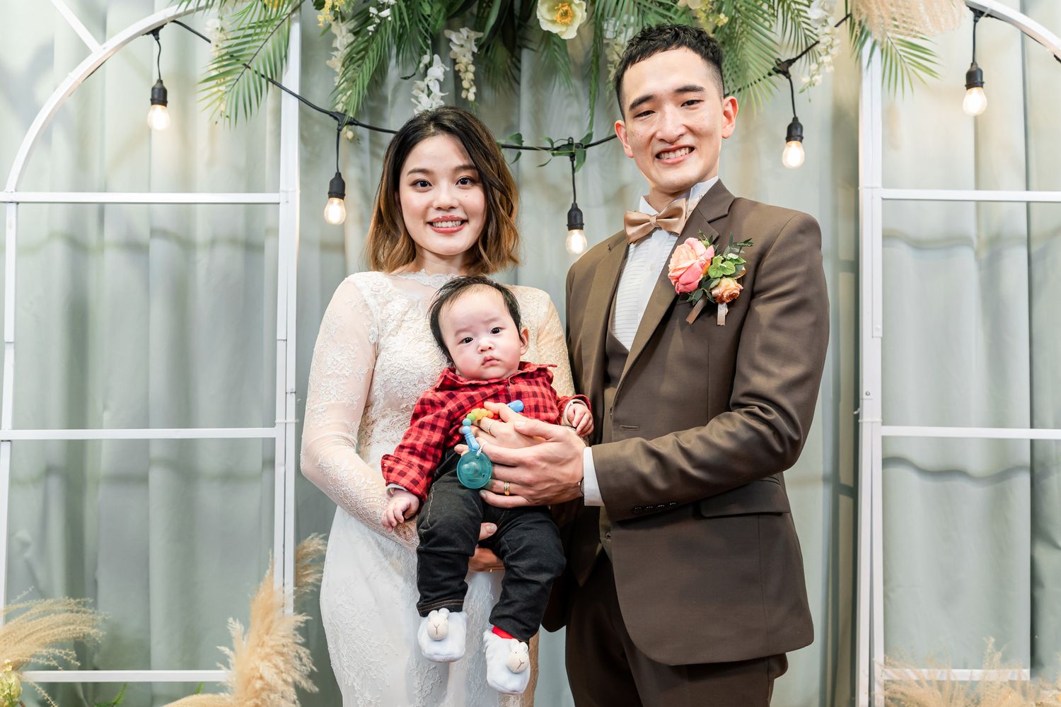 A family poses together at an elegant wedding ceremony with floral decor and string lights in the background.