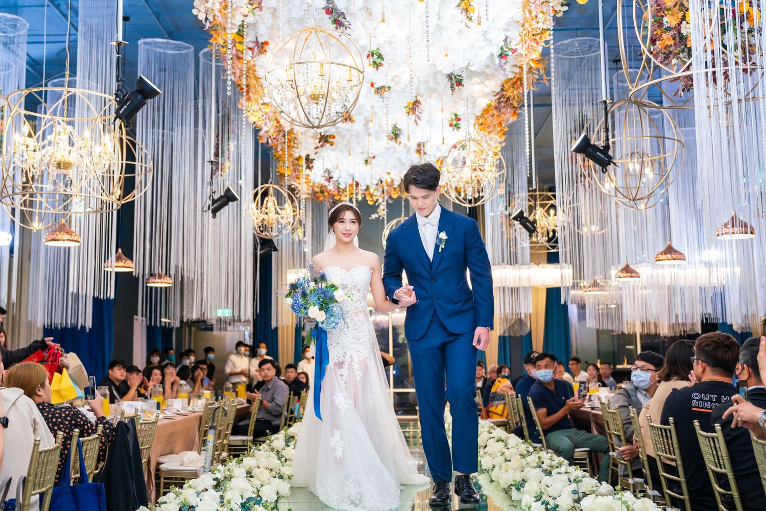 Elegant wedding venue decorated with crystal chandeliers and floral arrangements beneath glowing lights.