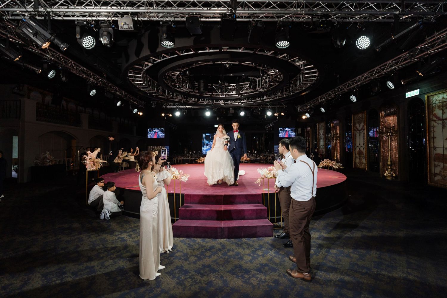A couple shares a special moment at their wedding reception in a dark venue with dramatic overhead lighting and stage setup.