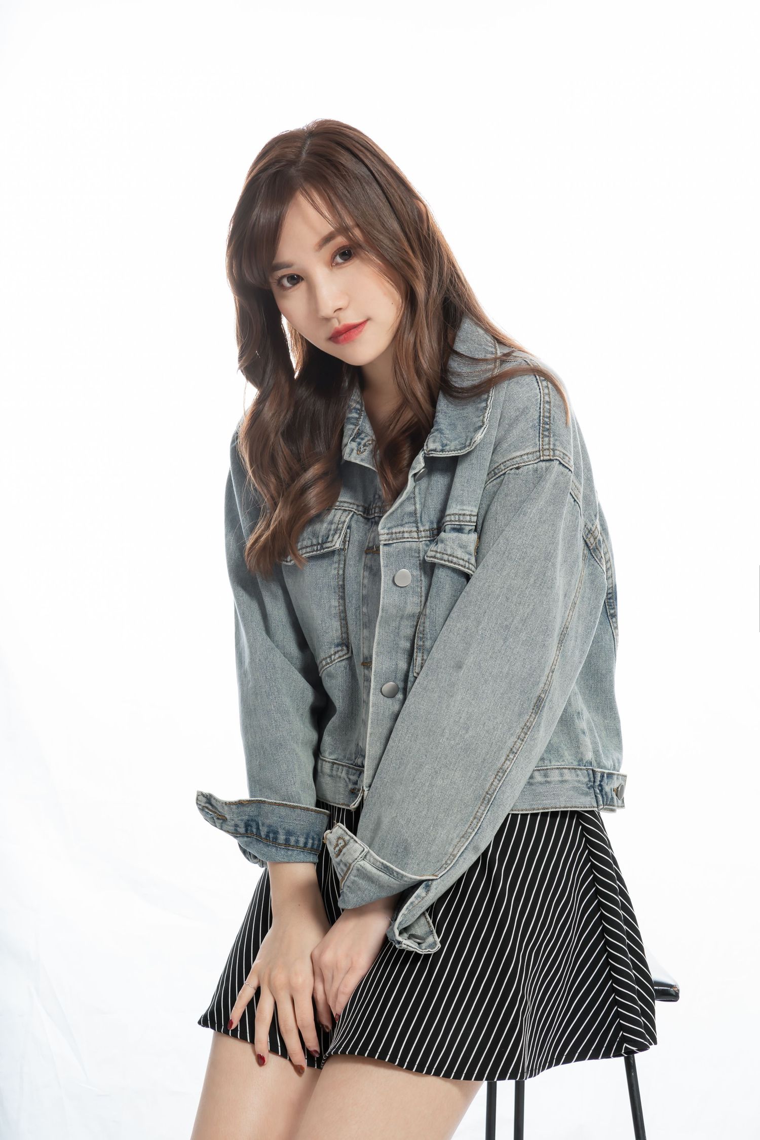 A model wearing a light denim jacket and black striped skirt poses against a white background for a fashion shoot.