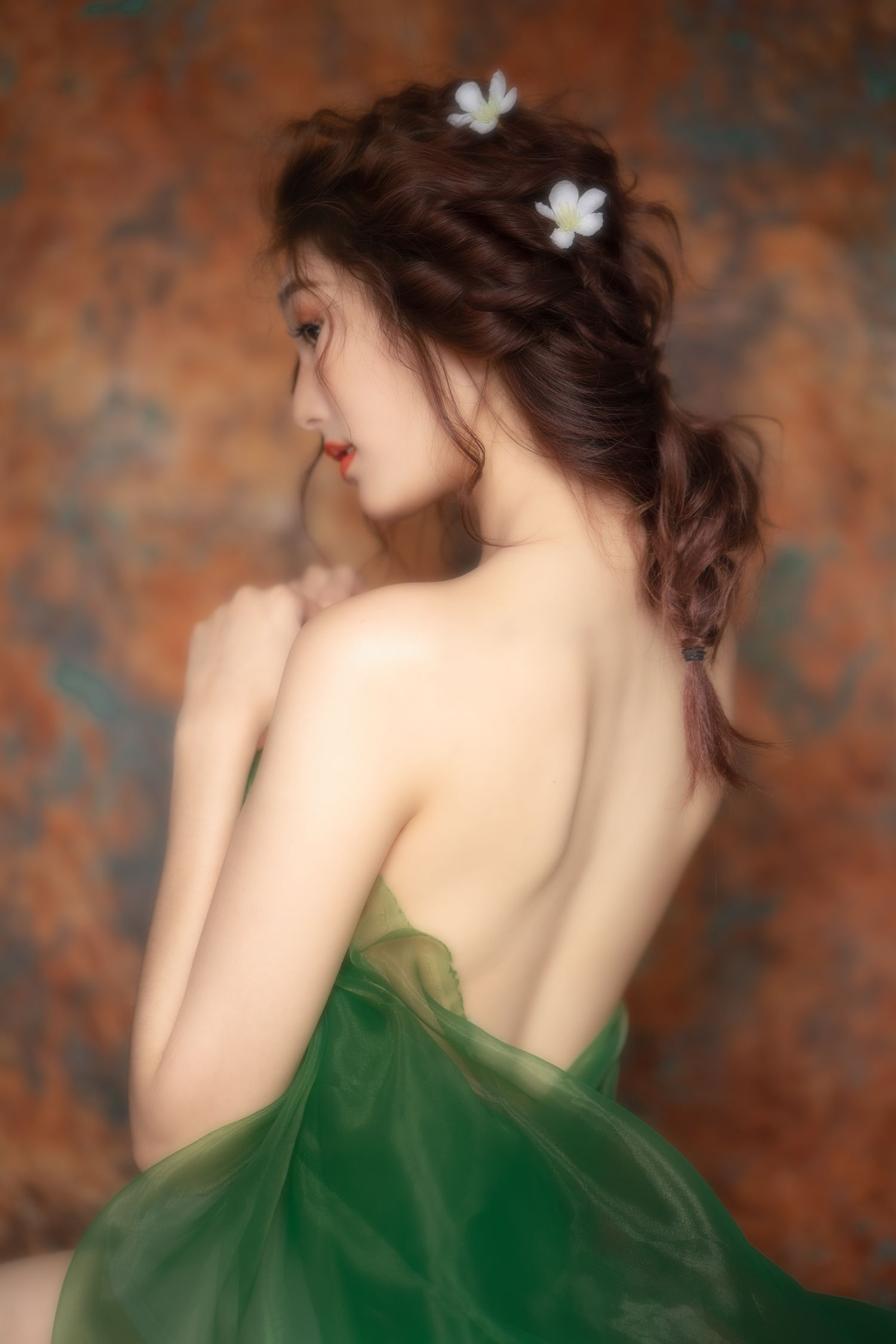 Elegant back view portrait showing bare shoulders draped in flowing green fabric with white floral hair accessories.