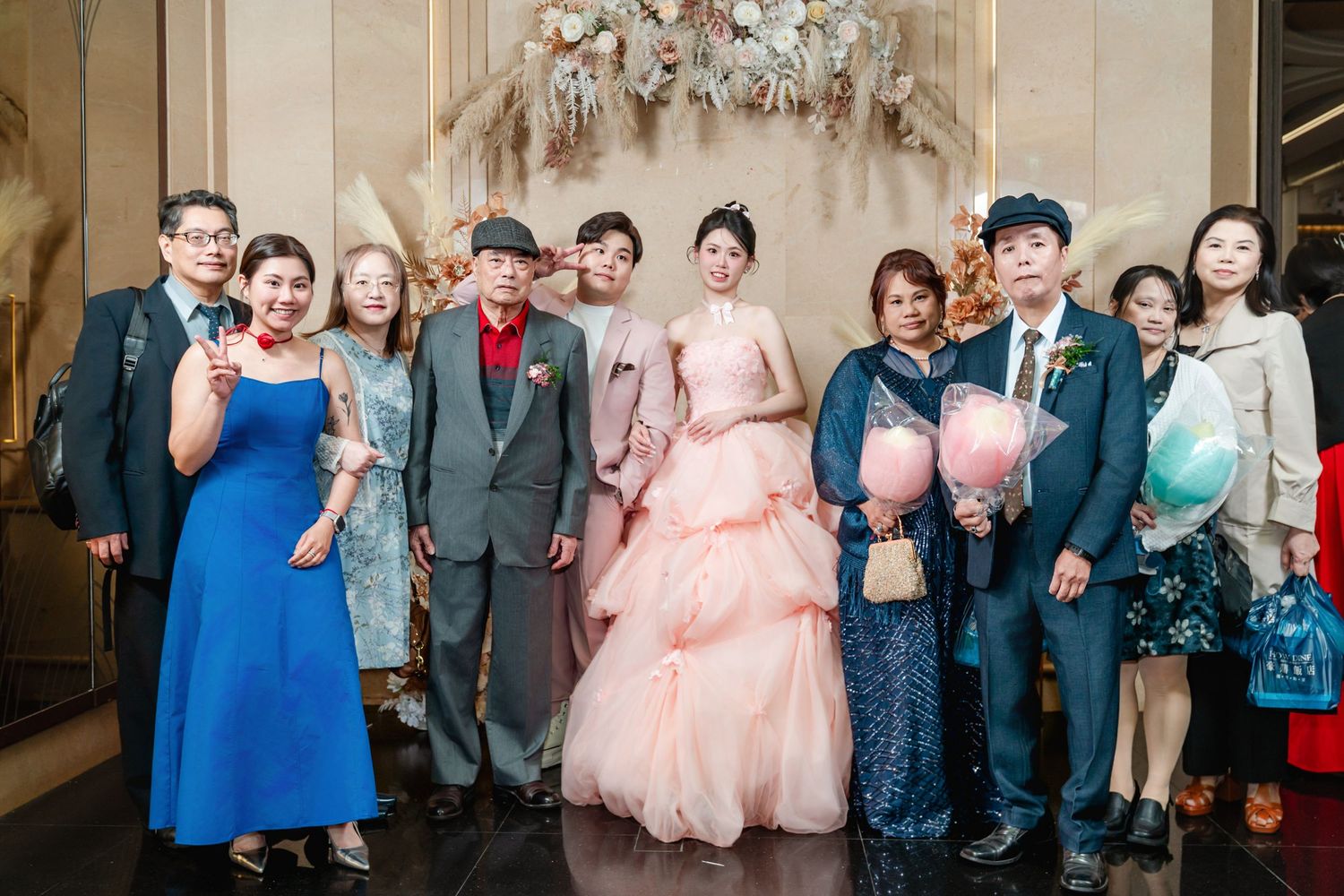 Wedding party group poses together at an elegant venue with the bride wearing a pink gown.