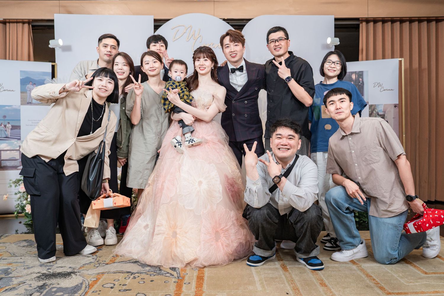 A bride and groom pose with smiling family and friends at a wedding reception in a elegant banquet hall.
