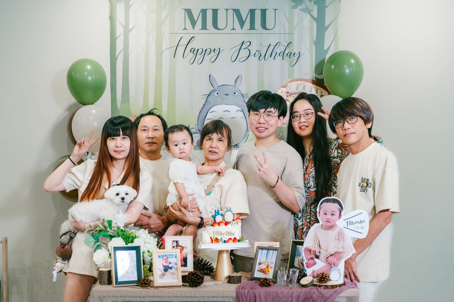 A group of people celebrate during a birthday party with green balloons and decorations in a festive setting.