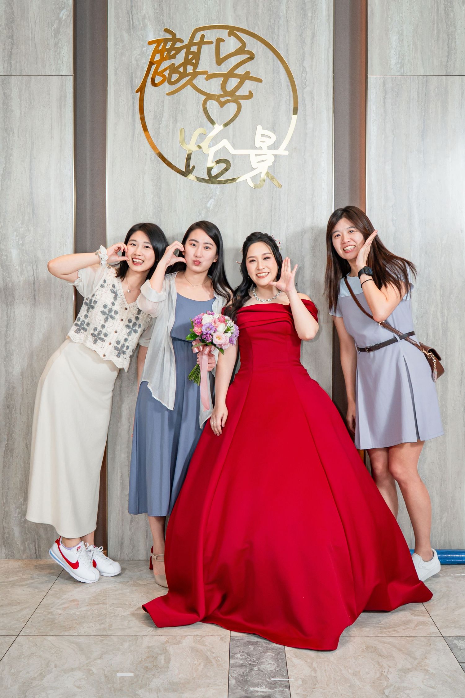 A joyful wedding celebration moment featuring a bride in red ballgown and friends in casual dresses posing playfully.