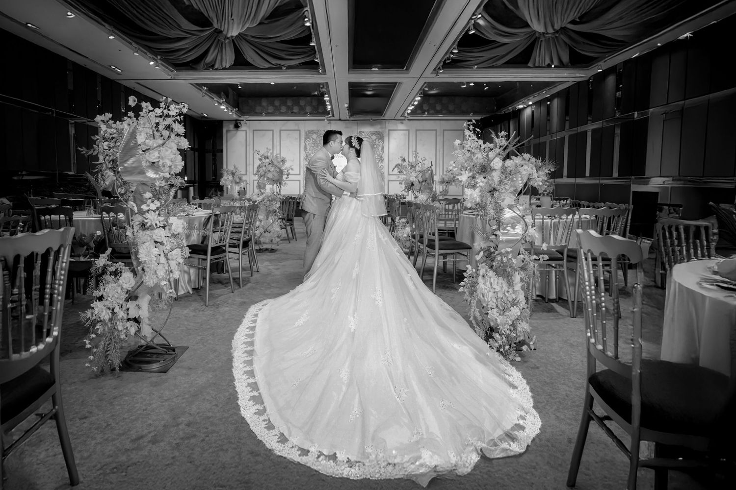 A stunning white ballgown wedding dress with intricate lace details and a flowing train photographed in a reception venue.