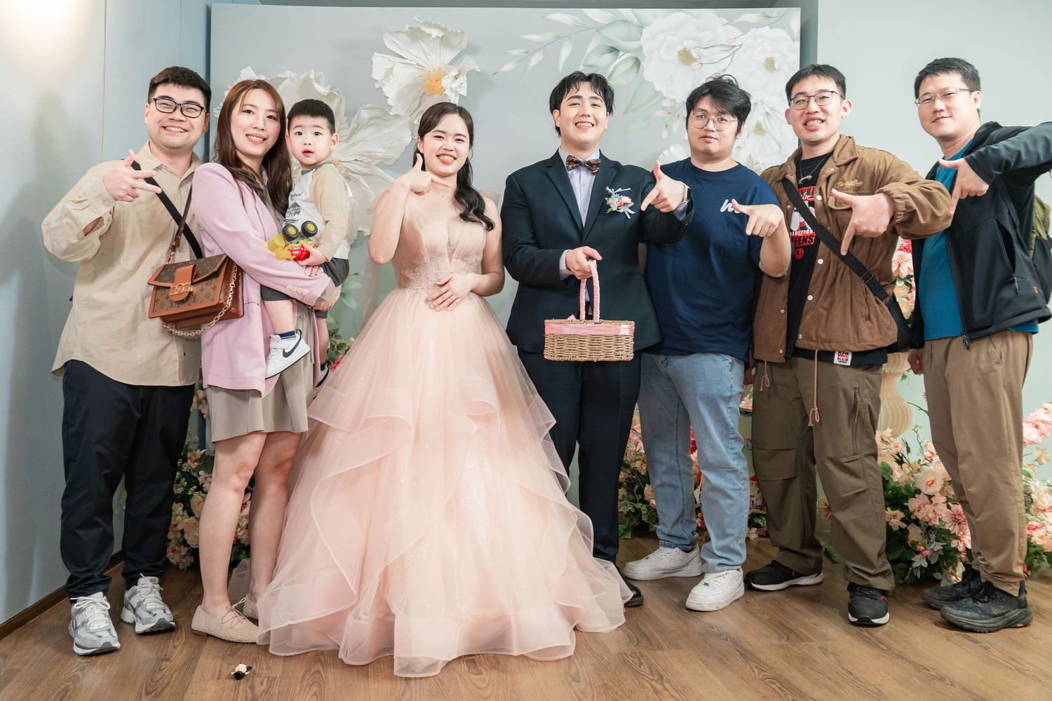 A group of friends pose together at a wedding celebration, with the bride wearing a pink tulle gown.