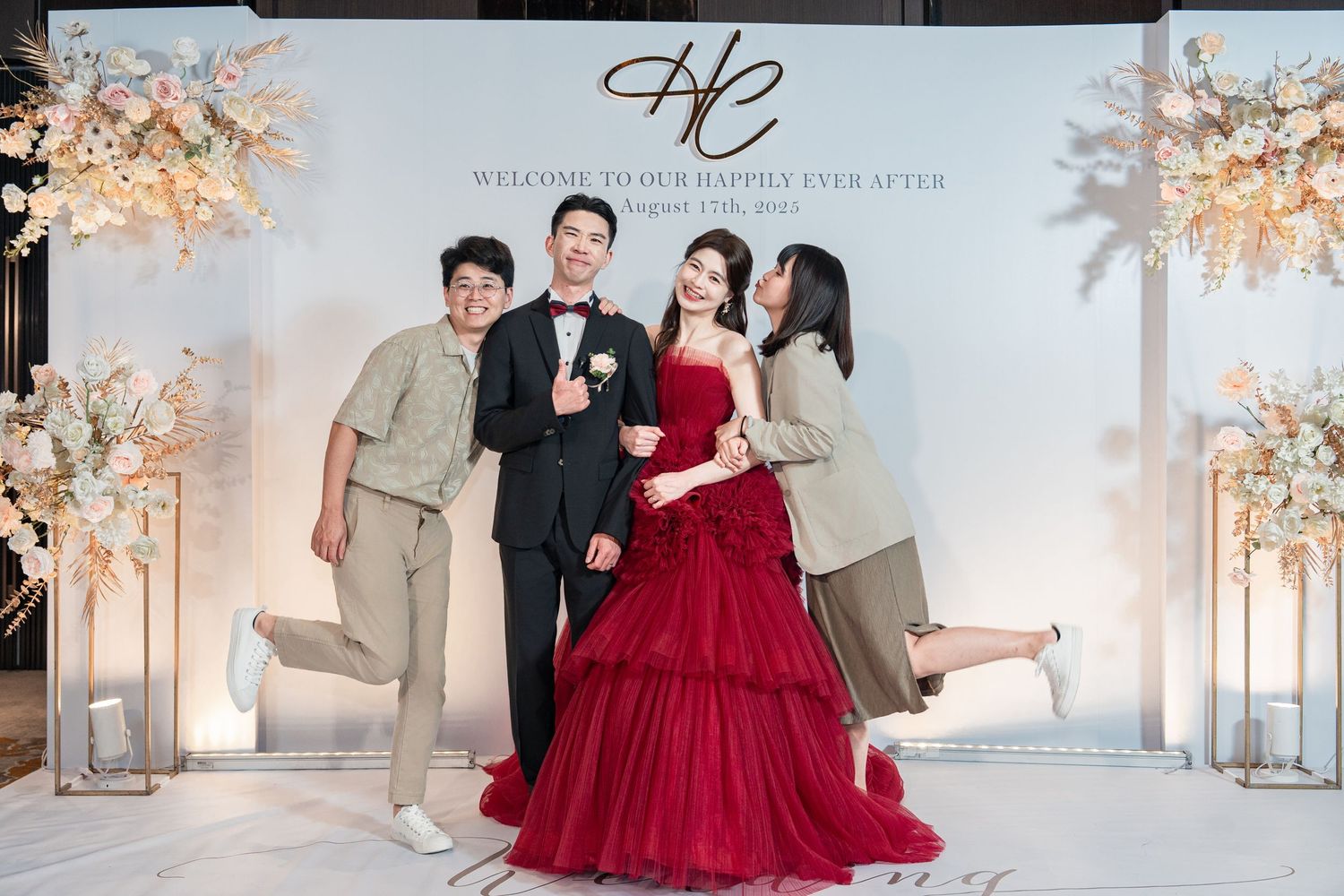 A group poses together at an elegant wedding backdrop with cherry blossom arrangements and a deep red ball gown.