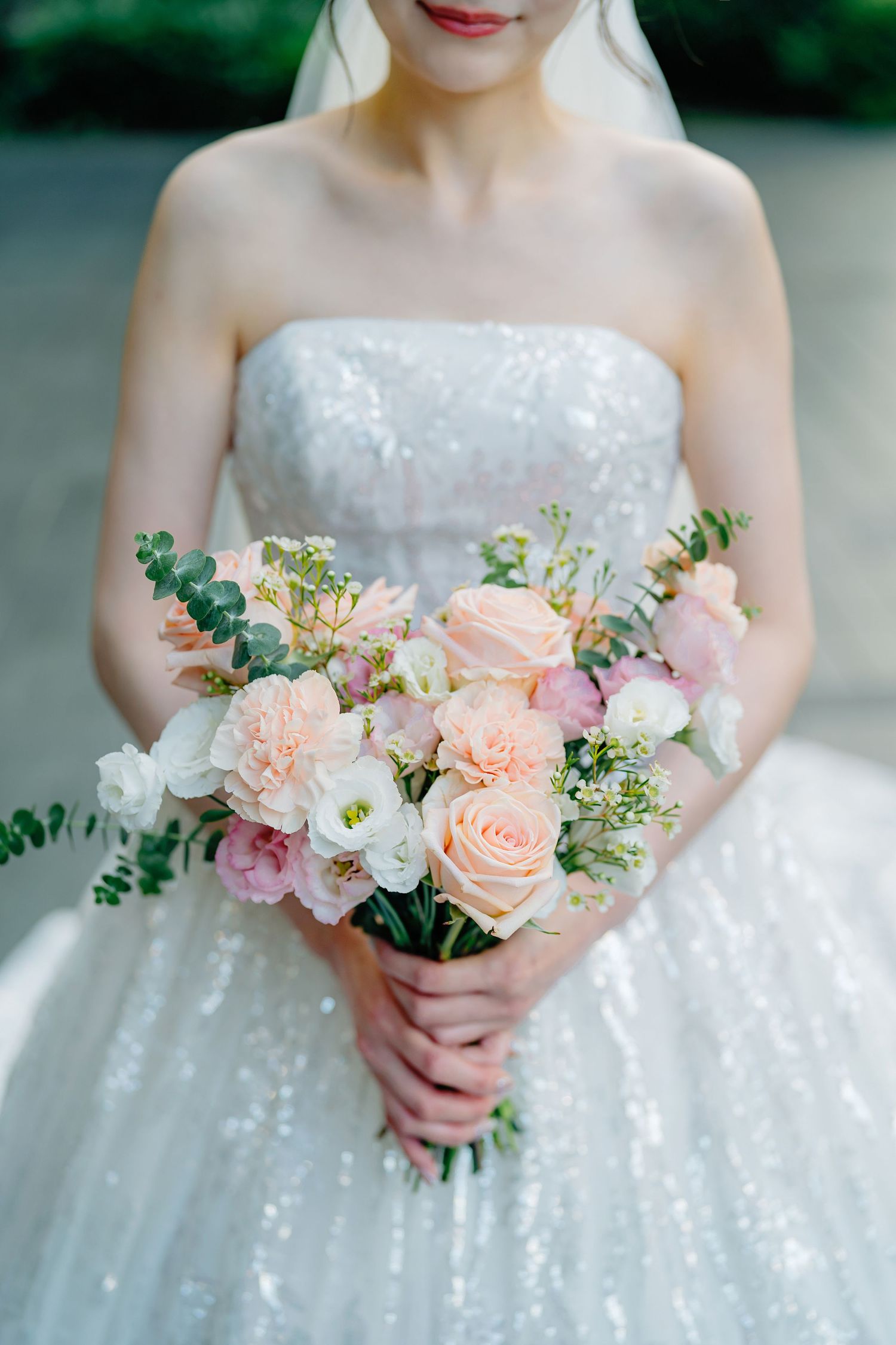 A romantic wedding bouquet of pink, peach and white roses with eucalyptus greens held against a sparkly white dress.