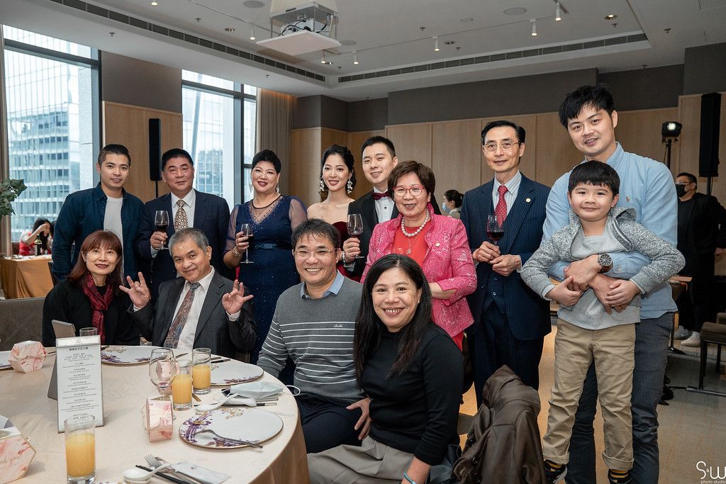 Casual group photo of wedding guests gathered around dining table at reception.