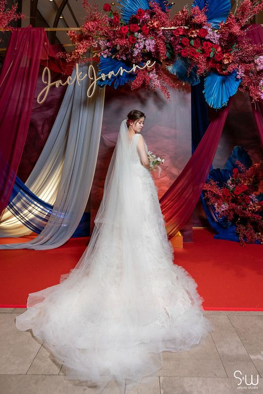 Bridal portrait against dramatic backdrop with red florals and flowing drapery.