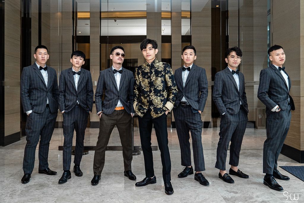 Seven groomsmen pose together in formal suits with one wearing a patterned jacket.