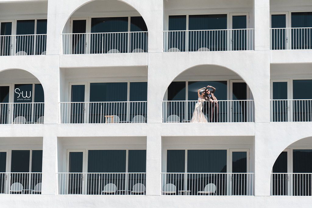 Wedding couple photographed on a white Mediterranean-style hotel balcony with arched architecture.