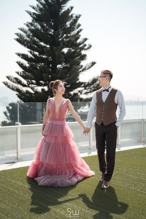 A romantic portrait of a couple walking on a rooftop garden with a tall pine tree in the background.